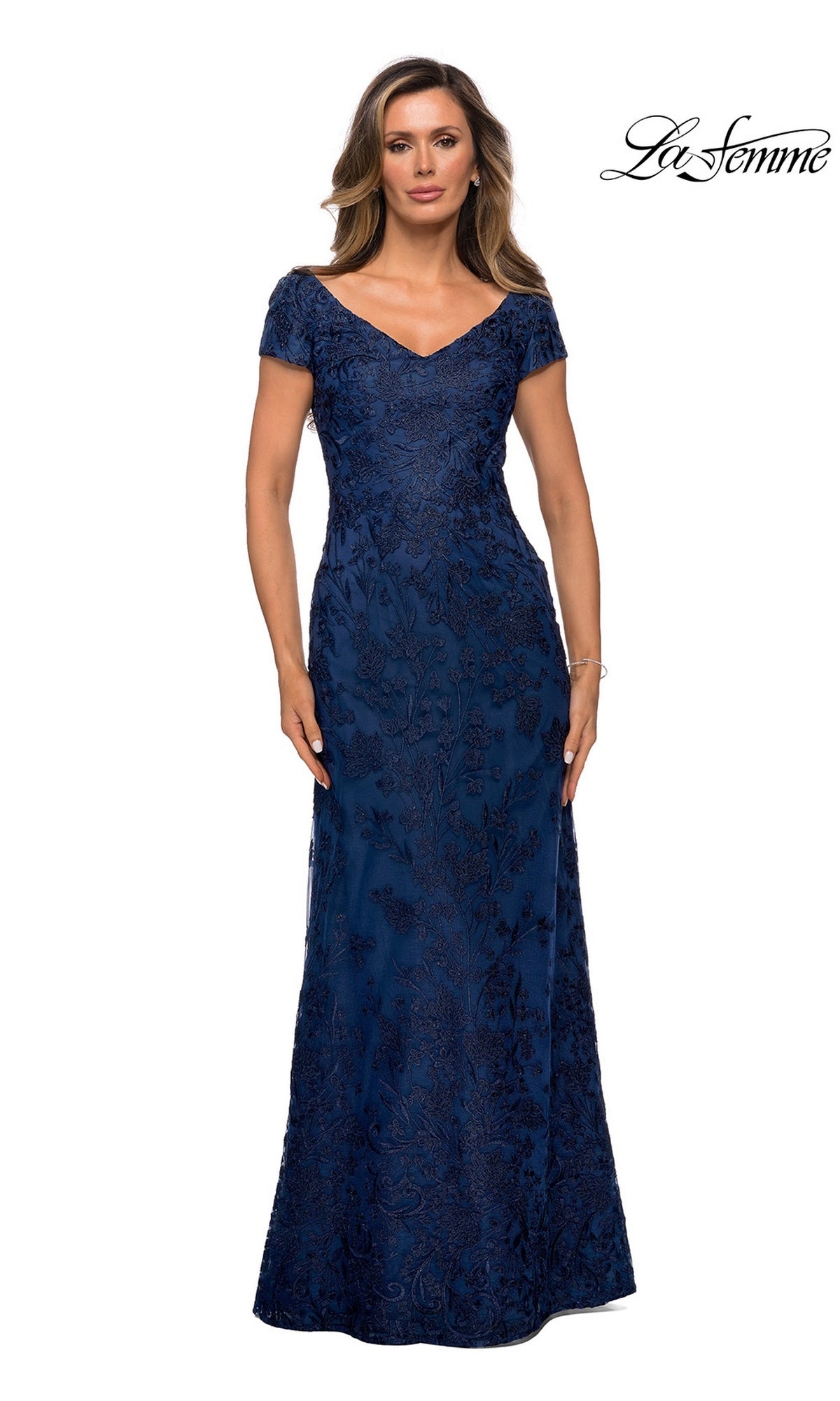 A woman in the Long Formal Dress: La Femme 27915, a floor-length dark blue modest lace dress with floral embroidery, stands against a white background.